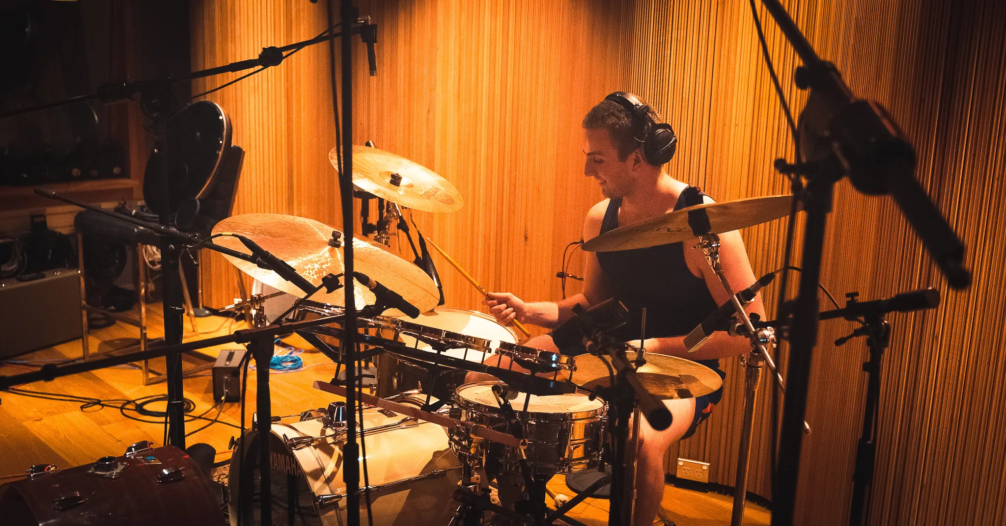 A drummer mid-take at a fully mic’d kit against the amber timber wall