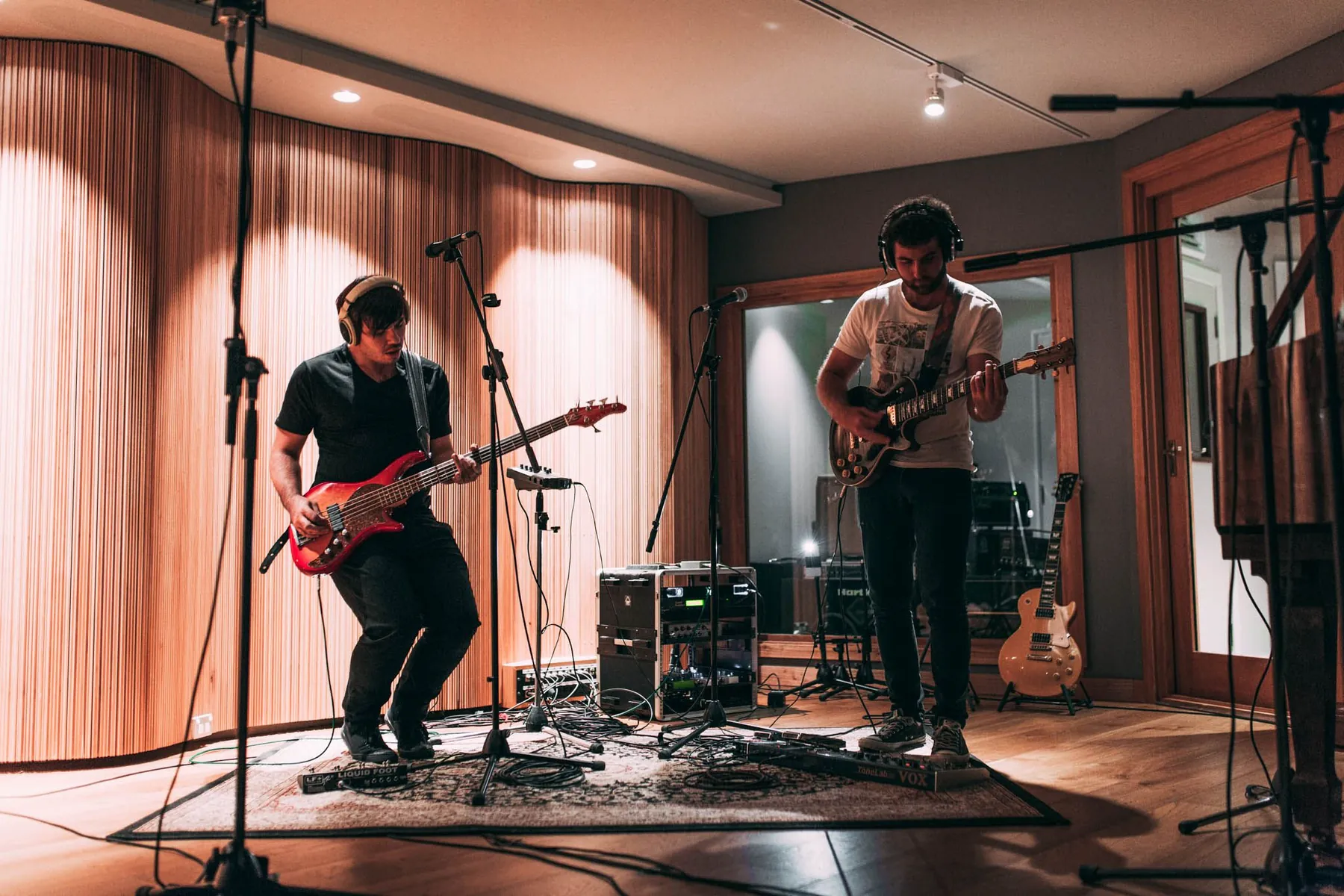 Two guitarists tracking together against the timber slat wall