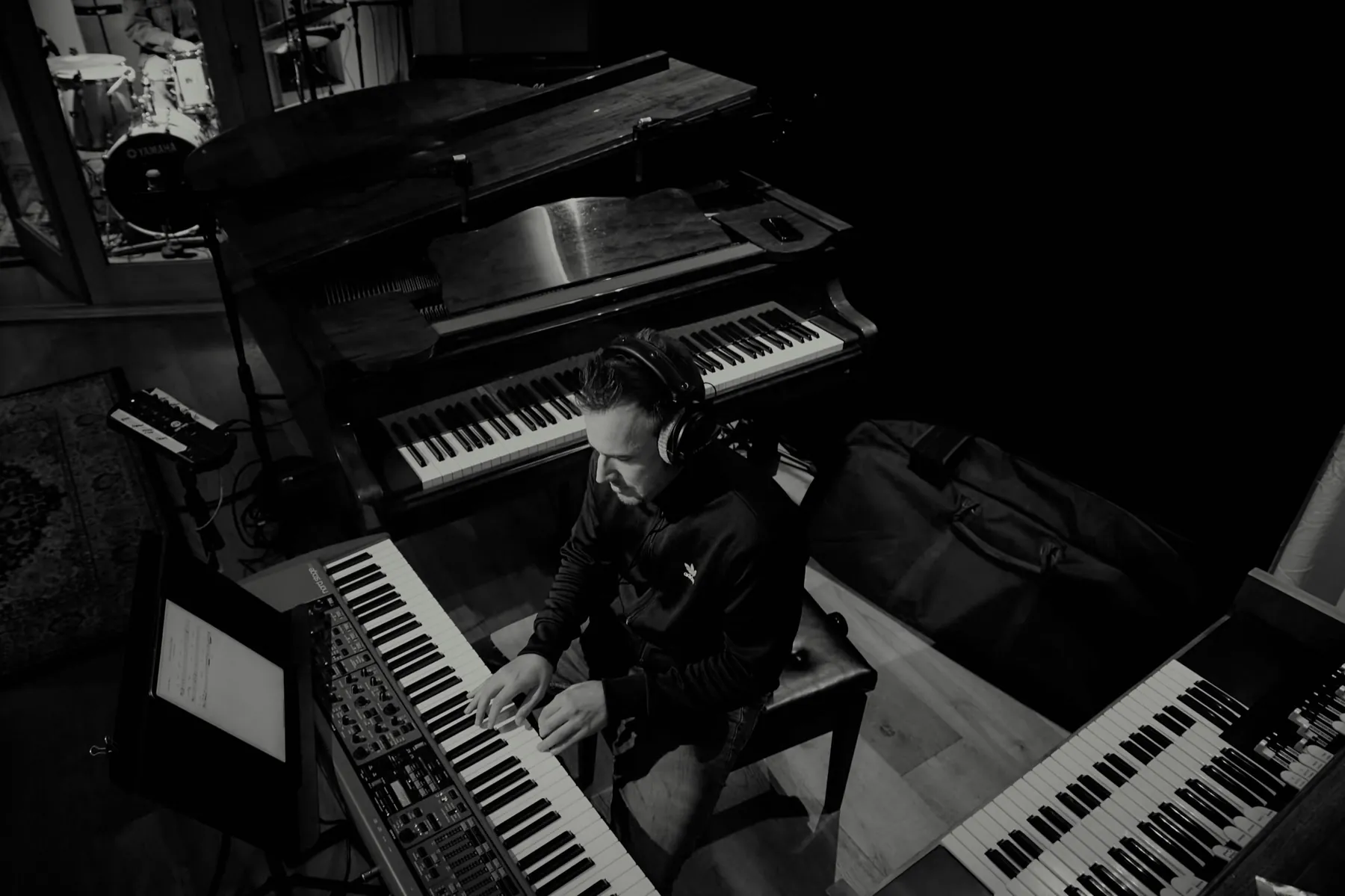 A keys player between the grand piano and synths, overhead in black and white