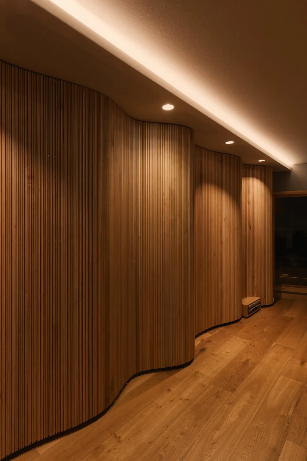 The curved timber slat wall under cove lighting